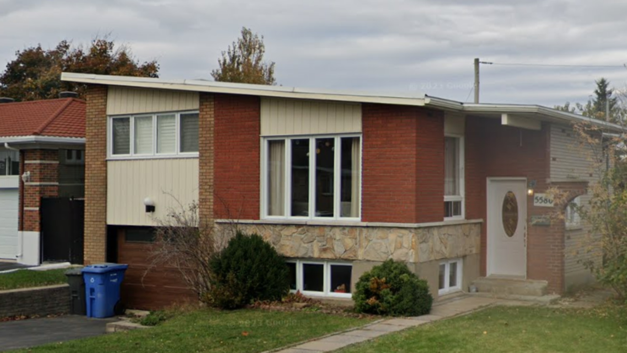 Maison en briques avec jardin et poubelles.
